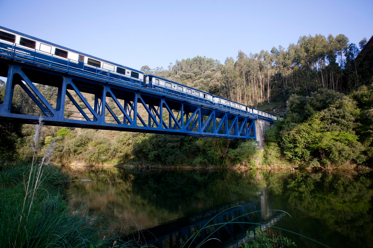 El Transcantabrico luxury train crossing blue steel bridge over river through forested landscape