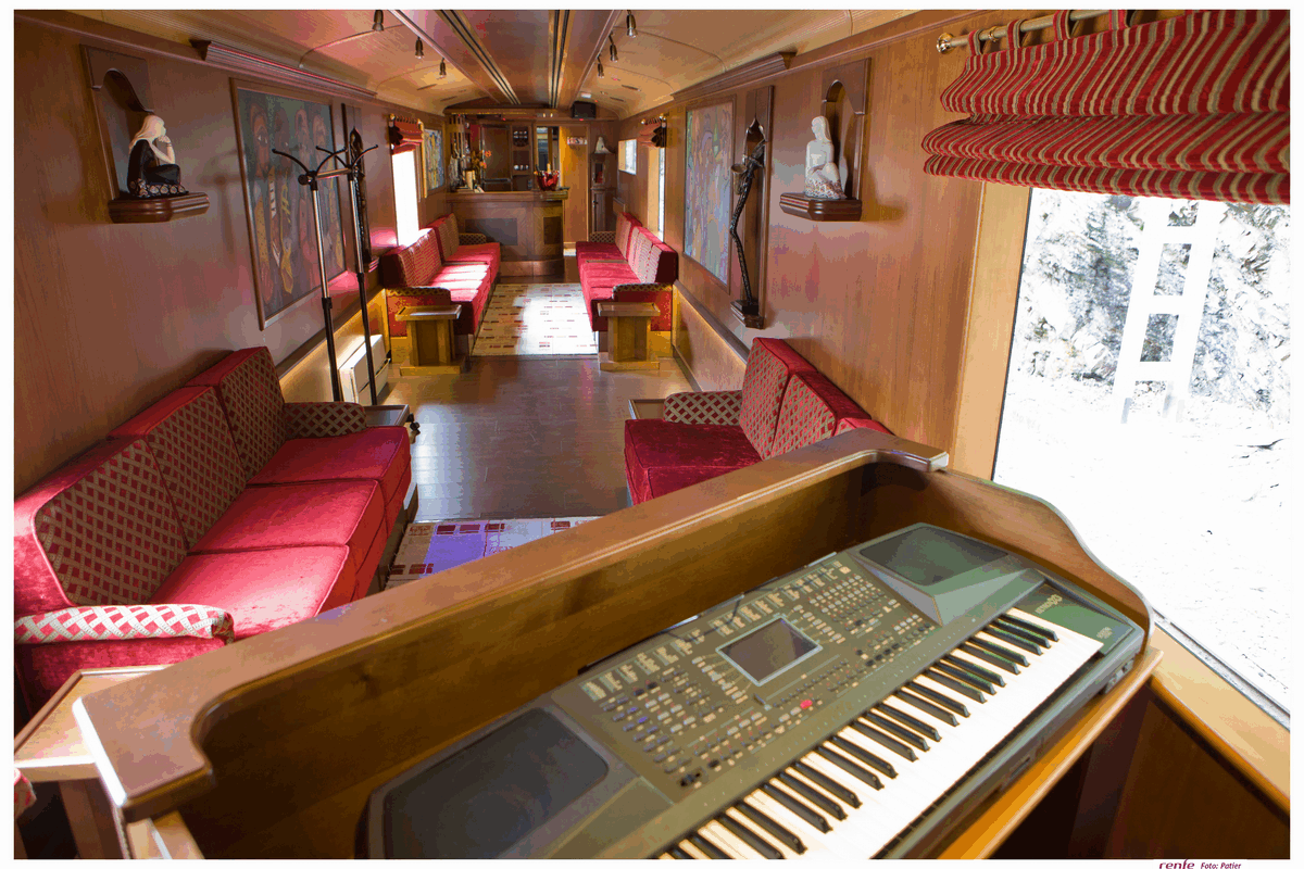 Luxury train lounge interior with red velvet seating, electronic piano, and elegant wood paneling